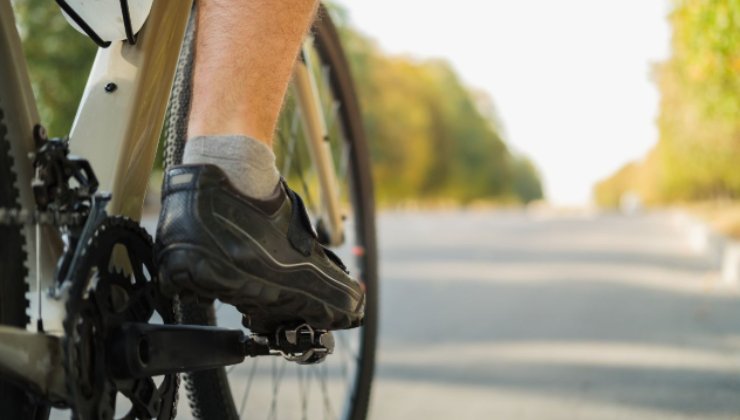 Il dettaglio di un piede sul pedale di una bici in strada