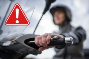 Una persona alla guida di uno scooter e il cartello rosso di allarme